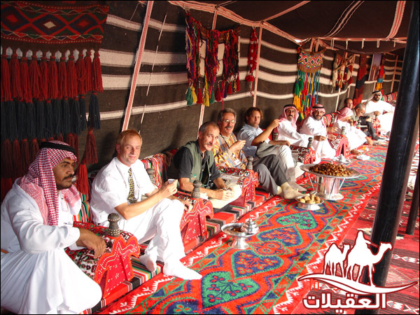 مجموعة من الأشخاص يجلسون في خيمة تقليدية مزينة بألوان زاهية، ويتناولون الطعام والمشروبات.