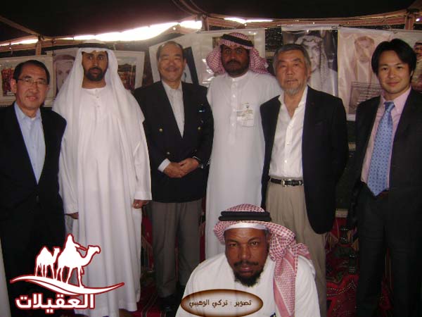 مجموعة من الرجال يقفون معًا في معرض، يرتدون أزياء مختلفة، وبعضهم يظهر بملابس تقليدية. الخلفية تحتوي على صور معروضة.