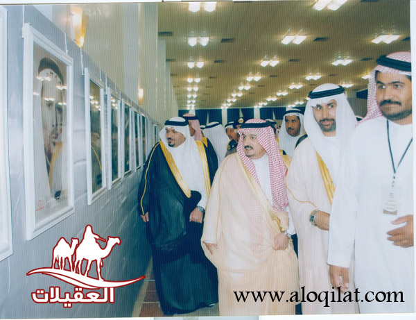 أفراد في معرض يتجولون أمام لوحات معروضة، يرتدون الملابس التقليدية.